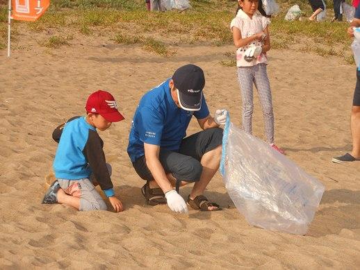 参加者の少年と一緒に浜辺のゴミを拾う市長の写真