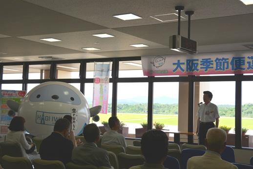 大阪便季節便運航初日セレモニーにて挨拶をする市長と耳を傾ける人たちの写真