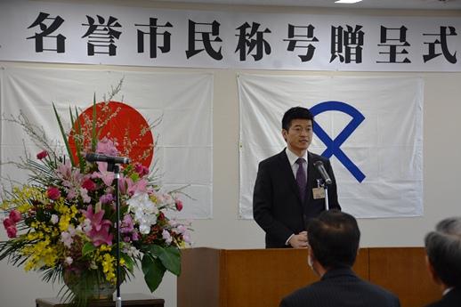 名誉市民称号贈呈式の壇上で市長があいさつしている様子の写真