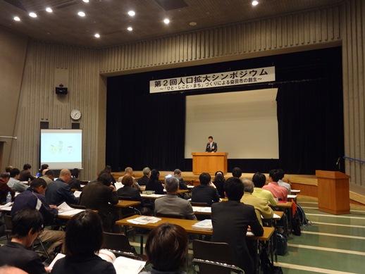 第2回人口拡大シンポジウム開会式での市長の話に耳を傾ける参加者たちの様子