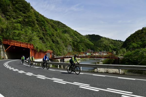 トンネルを抜け渓流沿いの道を自転車で走る参加者たち