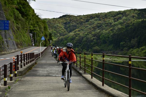 川沿いの道を自転車で並んで走る参加者たち