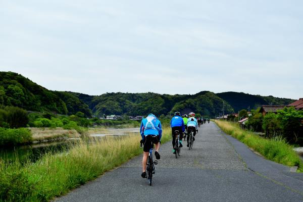 川沿いの土手道を自転車で走る参加者たちの後ろ姿
