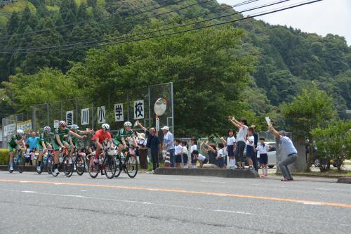 豊川小学校前を自転車で走る選手たちと声援を送る生徒たちの写真