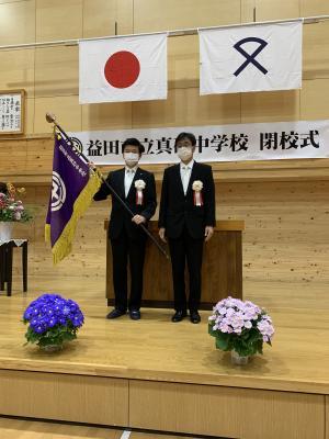 校旗を両手で持っている山本市長と小田校長の写真