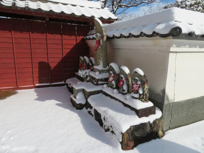 雪をかぶった山門前のお地蔵さんの写真