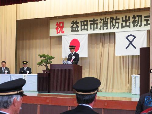 市民体育館壇上で出初式に参加している消防団員らの前で式辞を述べている団服姿の市長の写真