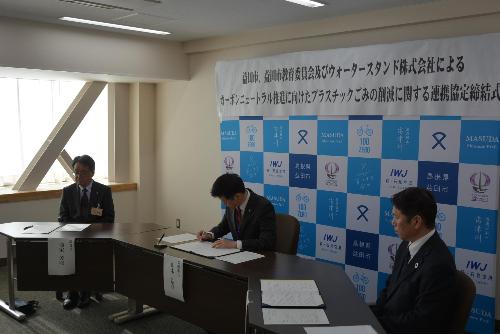 市役所大会議室で協定締結書に署名している市長の写真