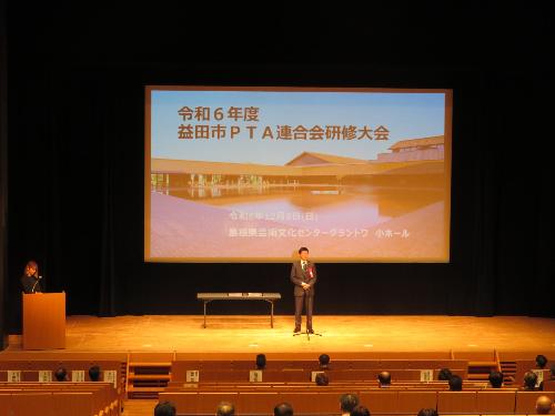 グラントワ小ホール壇上で研修会に集まったPTA役員らの前で挨拶をしている市長の写真