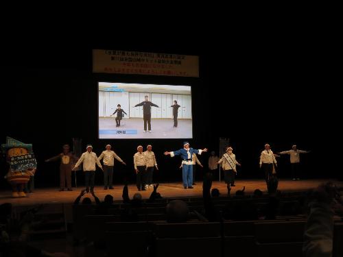 グラントワステージ上で市幹部職員や市議会議員らとともにますます元気体操を行っている市長の写真