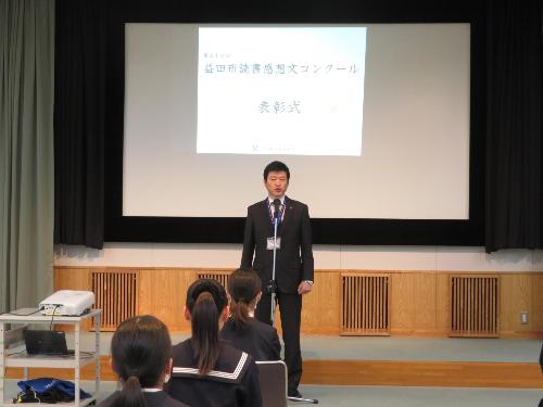 市立図書館視聴覚室でコンクール受章者らの前で祝辞を述べている市長の写真