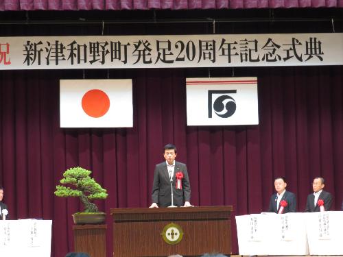 日原小学校体育館で行われた記念式典で壇上から出席者らに祝辞を述べている市長の写真