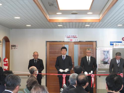 人権センターロビーで展示のテープカットを他の来賓と一緒に行う市長の写真