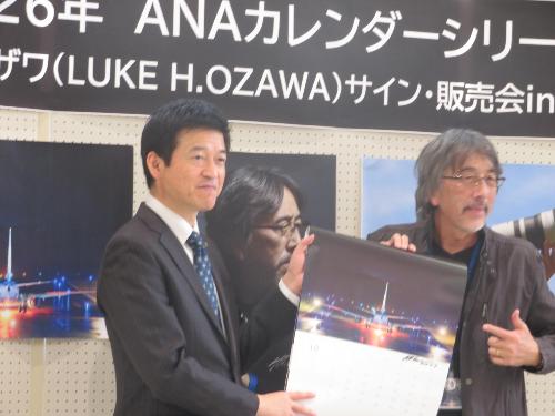 萩・石見空港ロビーで開かれたサイン会にルーク氏のサイン入り2026年カレンダーを同氏とともに持ち記念撮影に応じる市長の写真