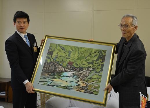 寄贈された切り絵の額を掲げる市長と三坂仁氏の写真