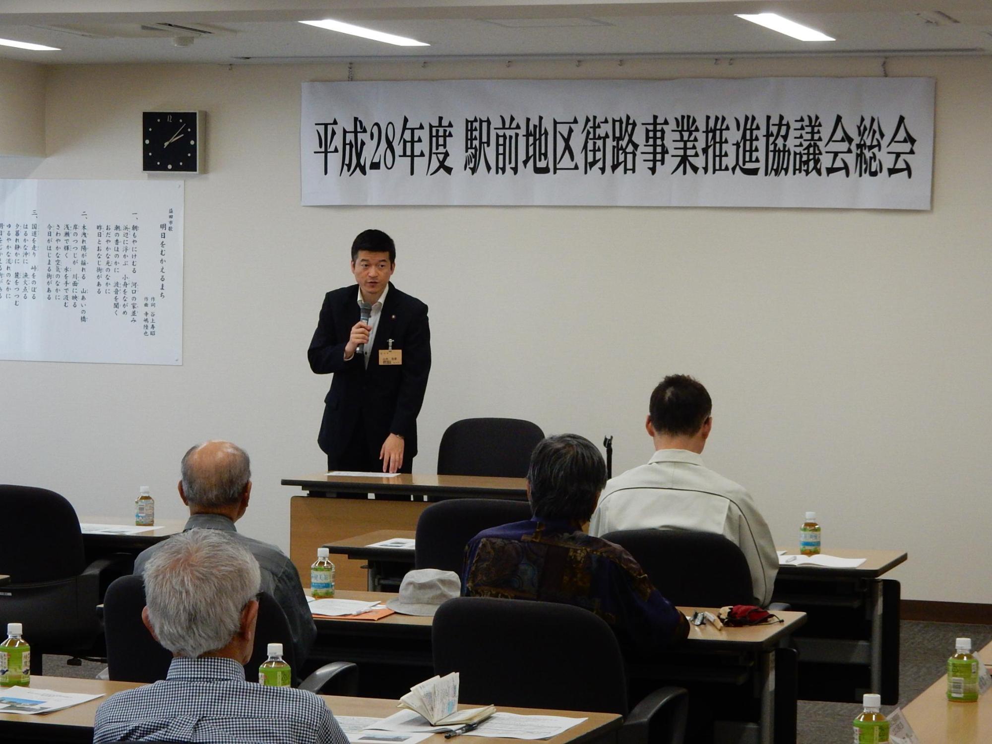 駅前地区街路事業推進協議会総会にてマイクを持って話す市長の様子の写真