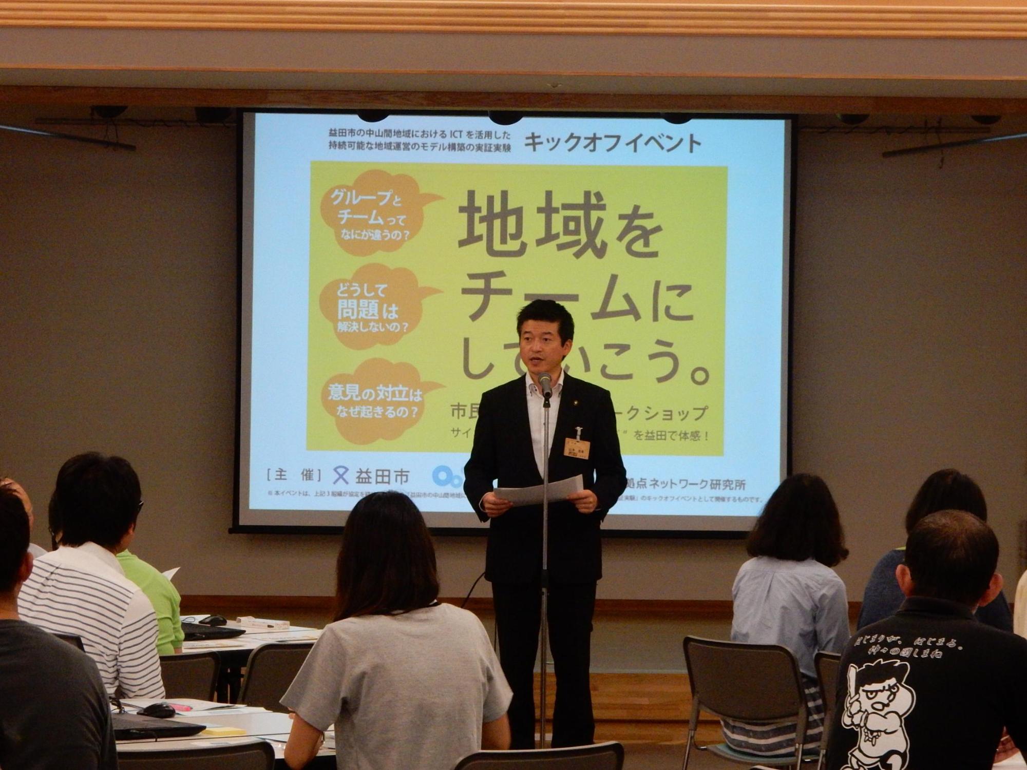 サイボウズ市民参加型ワークショップのステージにて挨拶を述べる市長と傾聴する参加者らの写真