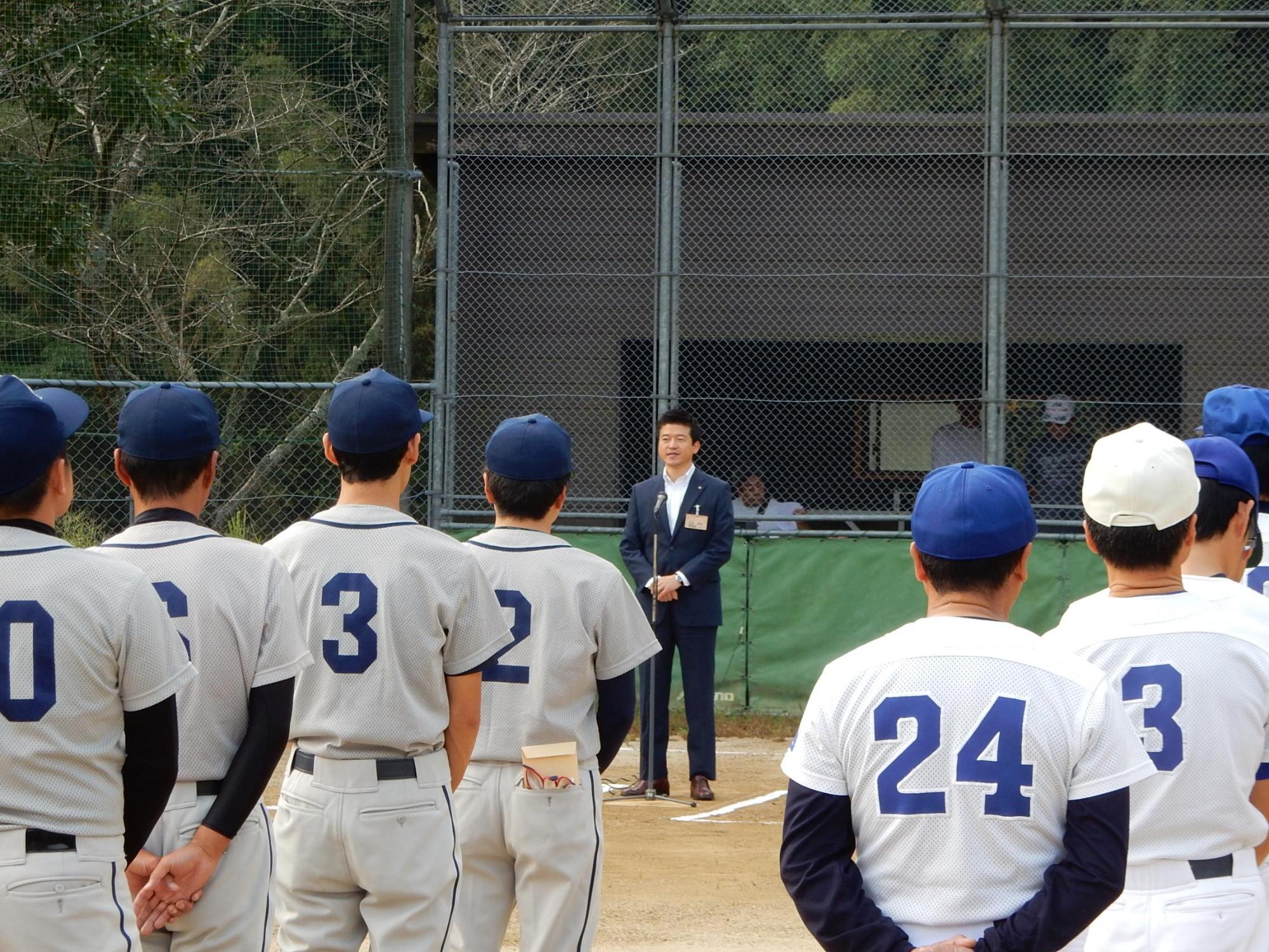 益田市市長杯ソフトボール大会にてグランドで挨拶を述べる市長と傾聴する選手らの写真