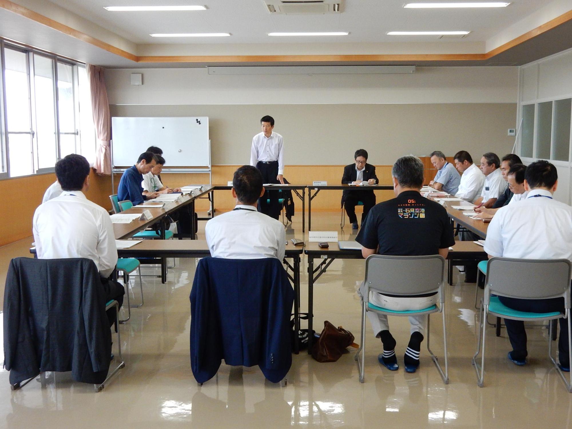 地域活性化総合特区地域協議会にて言葉を述べる市長と傾聴する出席者らの写真