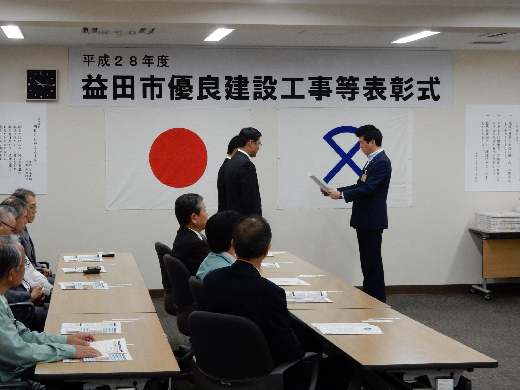 益田市優良建設工事等表彰式にて男性2名の前で賞状を読み上げる市長の写真