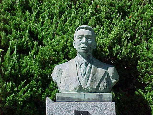 緑の木々の前にどっしりと置かれた秦佐八郎博士胸像の写真